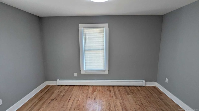 spare room featuring a baseboard heating unit, light wood-style flooring, and baseboards