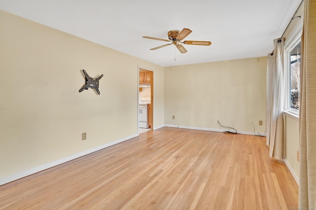 spare room featuring light wood finished floors, a ceiling fan, and baseboards