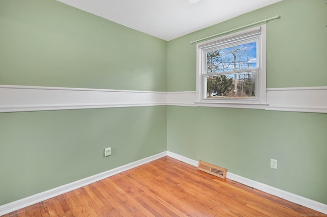 unfurnished room featuring wood finished floors, visible vents, and baseboards