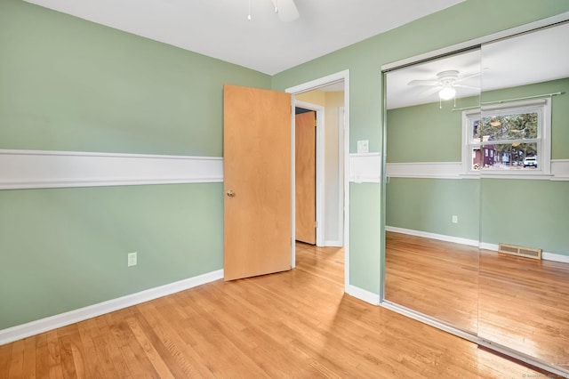 unfurnished bedroom with a closet, visible vents, a ceiling fan, wood finished floors, and baseboards