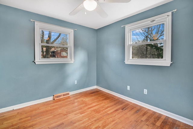 unfurnished room featuring a healthy amount of sunlight, visible vents, baseboards, and wood finished floors