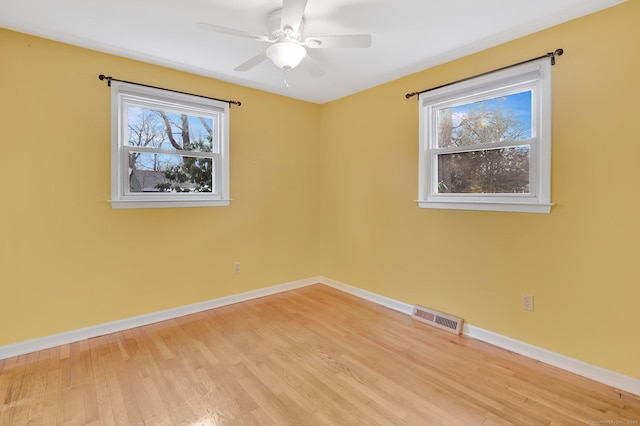 empty room featuring a healthy amount of sunlight, baseboards, visible vents, and light wood-style flooring