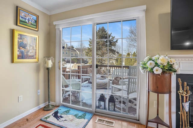 doorway to outside featuring ornamental molding, wood finished floors, visible vents, and baseboards