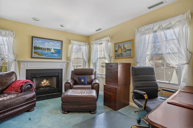 carpeted office featuring a fireplace with flush hearth, visible vents, and baseboards