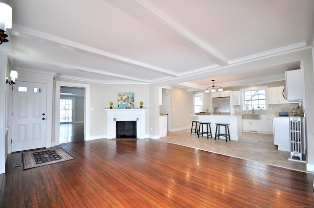 unfurnished living room with a fireplace, a sink, baseboards, light wood-style floors, and beamed ceiling