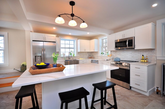 kitchen featuring a breakfast bar, stainless steel appliances, backsplash, white cabinetry, and light stone countertops