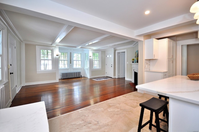 kitchen featuring a fireplace, white cabinetry, open floor plan, beam ceiling, and radiator