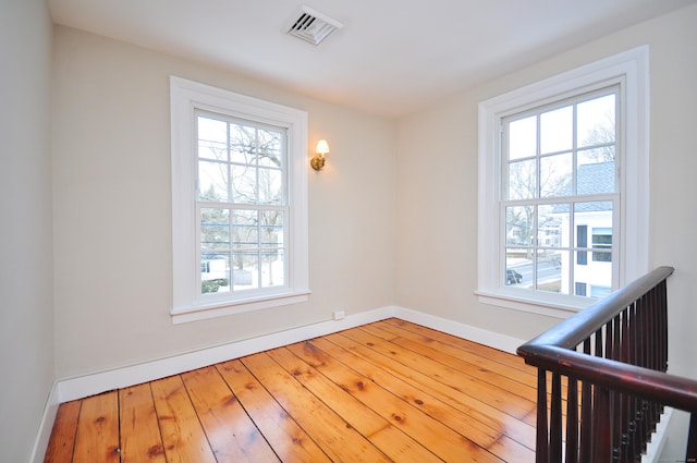 empty room featuring wood-type flooring, visible vents, and baseboards