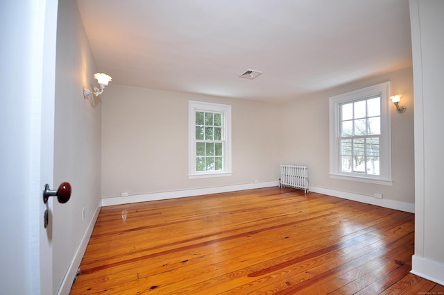 unfurnished room featuring radiator, hardwood / wood-style flooring, plenty of natural light, and visible vents