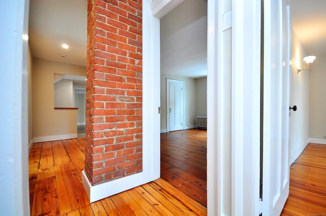 hall with brick wall, radiator heating unit, hardwood / wood-style flooring, and baseboards