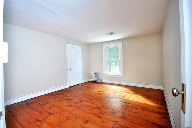 unfurnished room with visible vents, radiator heating unit, hardwood / wood-style flooring, and baseboards