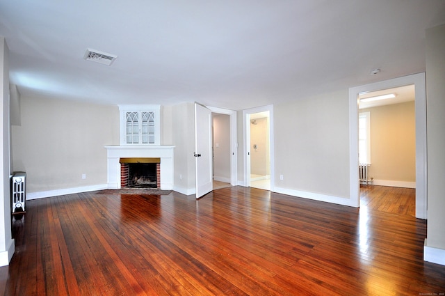 unfurnished living room featuring hardwood / wood-style flooring, visible vents, baseboards, a brick fireplace, and radiator heating unit