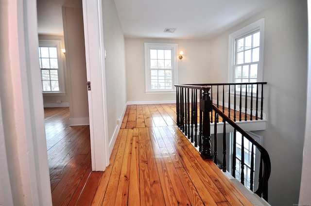 hallway with light wood-type flooring, an upstairs landing, visible vents, and baseboards