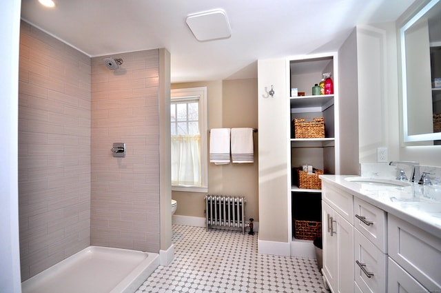 bathroom featuring toilet, radiator heating unit, a tile shower, vanity, and baseboards