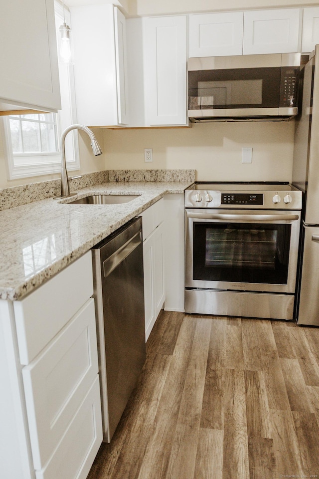 kitchen with white cabinets, light wood-style flooring, stainless steel appliances, and a sink