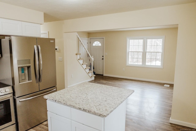 kitchen featuring light stone counters, appliances with stainless steel finishes, white cabinets, a kitchen island, and light wood-type flooring