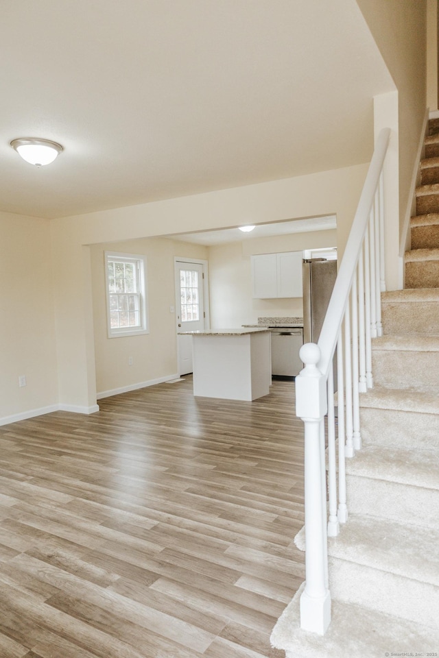 unfurnished living room with light wood-style floors, stairs, and baseboards