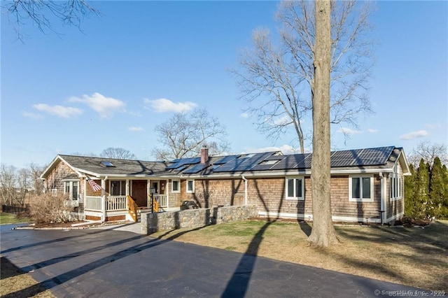 ranch-style house featuring a chimney, a porch, and roof mounted solar panels