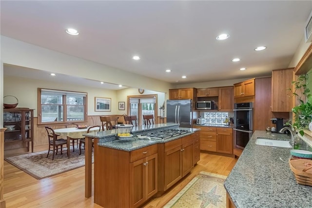 kitchen with light wood finished floors, stainless steel appliances, stone countertops, wainscoting, and a sink