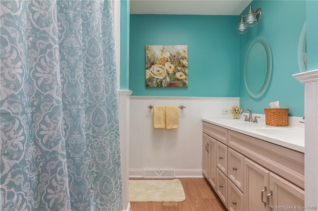 bathroom featuring double vanity, a wainscoted wall, a sink, and wood finished floors