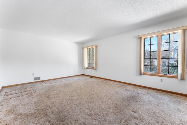 carpeted empty room featuring baseboards, visible vents, and a textured ceiling