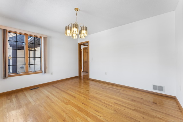 empty room featuring an inviting chandelier, light wood-type flooring, visible vents, and baseboards