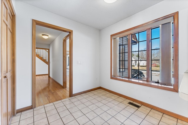 spare room with visible vents, stairway, baseboards, and light tile patterned flooring