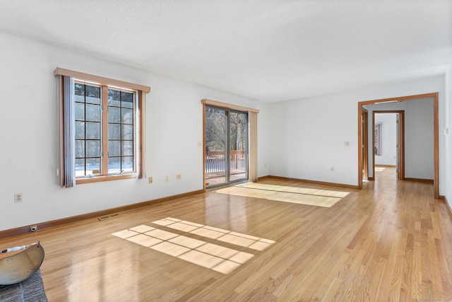 unfurnished room with baseboards, a textured ceiling, visible vents, and light wood-style floors