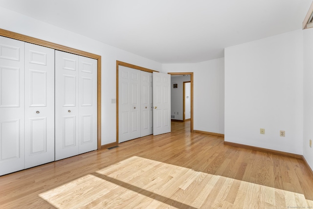 unfurnished bedroom with baseboards, two closets, and wood finished floors