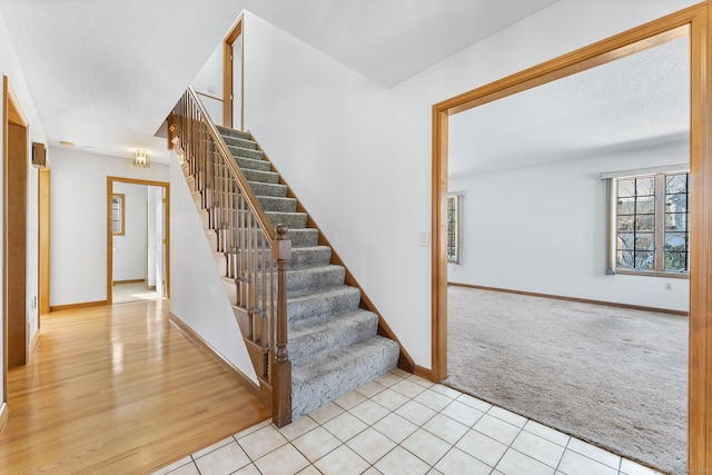 stairway with carpet floors, tile patterned flooring, a textured ceiling, and baseboards