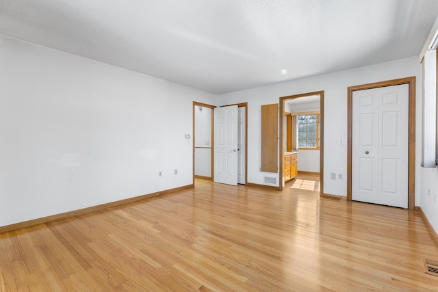 unfurnished bedroom featuring light wood-style floors, visible vents, baseboards, and ensuite bathroom