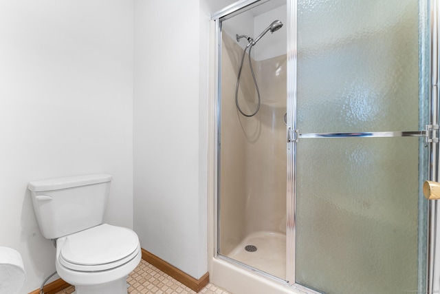 bathroom featuring toilet, a stall shower, and baseboards