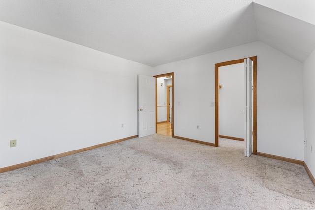 interior space featuring carpet flooring, vaulted ceiling, a textured ceiling, and baseboards