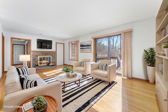 living room featuring a brick fireplace, light wood-style flooring, and baseboards