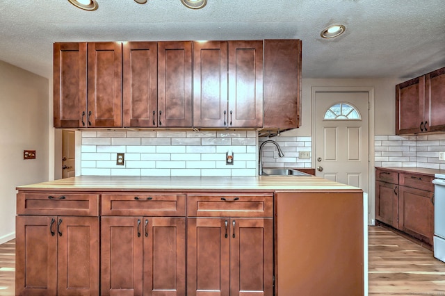 kitchen with a sink, light wood-style floors, light countertops, decorative backsplash, and white electric range oven