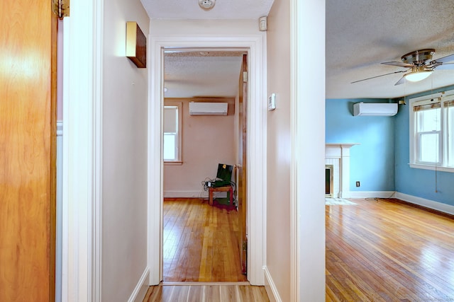 hall featuring a wall mounted air conditioner, a textured ceiling, and hardwood / wood-style floors