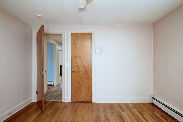 spare room featuring light wood finished floors, baseboards, a baseboard heating unit, and a textured ceiling