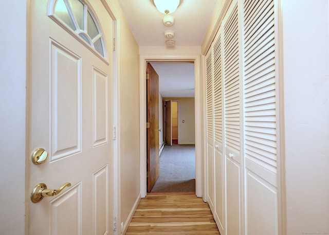 hallway with a textured ceiling, light wood finished floors, and baseboards