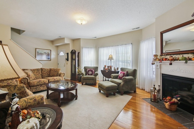 living room featuring a fireplace with flush hearth, a textured ceiling, wood finished floors, and visible vents