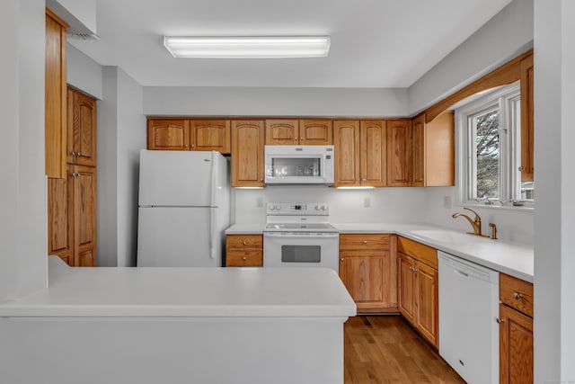 kitchen with light countertops, white appliances, a sink, and light wood-style floors