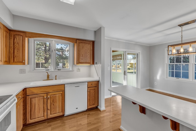 kitchen with brown cabinets, light countertops, hanging light fixtures, a sink, and white appliances