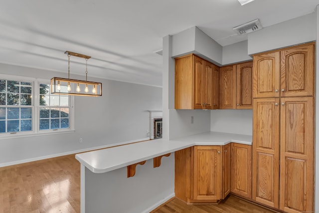 kitchen featuring a peninsula, visible vents, light countertops, brown cabinetry, and decorative light fixtures