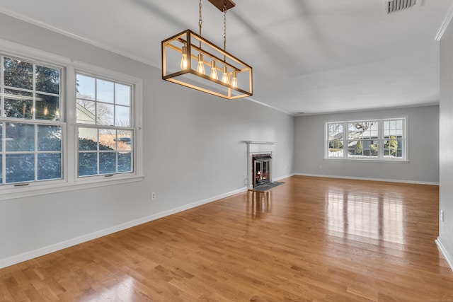 unfurnished living room with visible vents, a fireplace with flush hearth, ornamental molding, wood finished floors, and baseboards