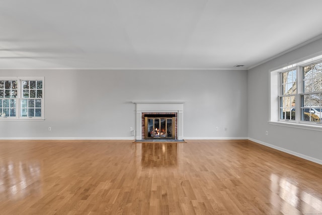 unfurnished living room with a fireplace, visible vents, baseboards, ornamental molding, and light wood-type flooring