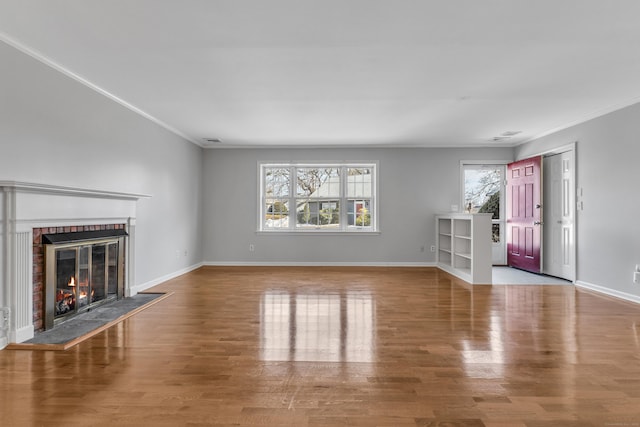 unfurnished living room with a brick fireplace, plenty of natural light, baseboards, and wood finished floors