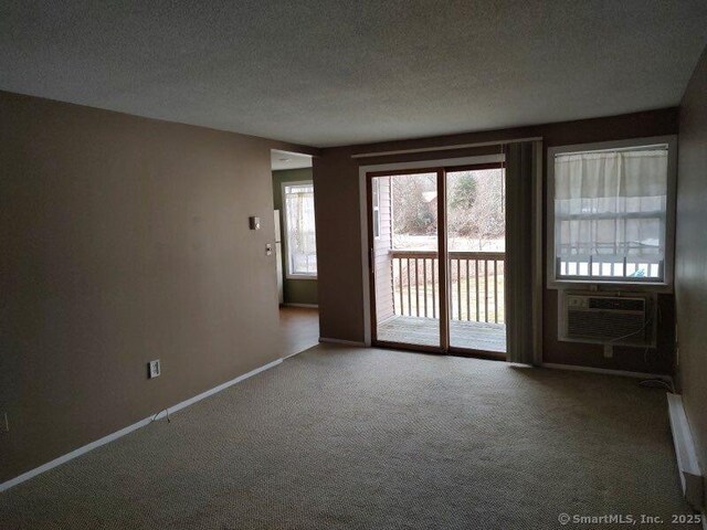 carpeted spare room with a textured ceiling, a wall mounted air conditioner, and baseboards