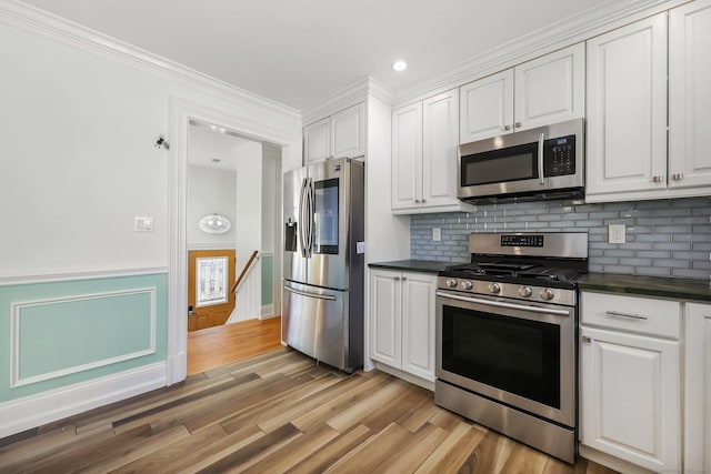 kitchen with stainless steel appliances, white cabinetry, wainscoting, light wood finished floors, and dark countertops