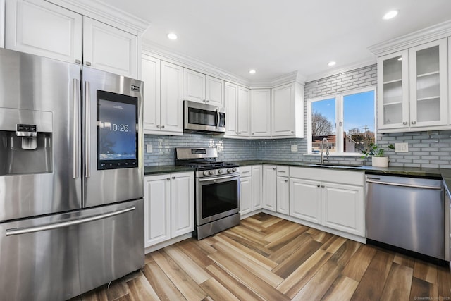 kitchen with a sink, white cabinets, appliances with stainless steel finishes, dark countertops, and glass insert cabinets