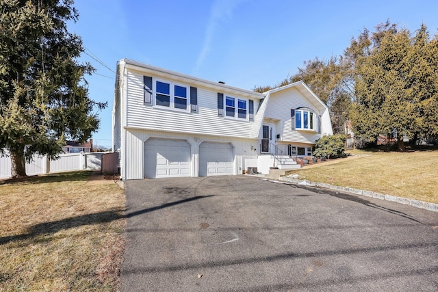 bi-level home with aphalt driveway, a front yard, fence, and a garage