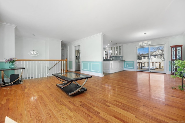 unfurnished living room featuring crown molding, wainscoting, light wood-type flooring, and an inviting chandelier